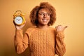 Young beautiful African American afro woman with curly hair holding vintage alarm clock pointing and showing with thumb up to the Royalty Free Stock Photo