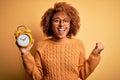Young beautiful African American afro woman with curly hair holding vintage alarm clock screaming proud and celebrating victory Royalty Free Stock Photo