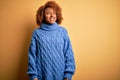 Young beautiful African American afro woman with curly hair wearing blue turtleneck sweater looking away to side with smile on Royalty Free Stock Photo