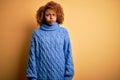 Young beautiful African American afro woman with curly hair wearing blue turtleneck sweater puffing cheeks with funny face Royalty Free Stock Photo