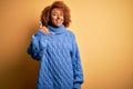 Young beautiful African American afro woman with curly hair wearing blue turtleneck sweater smiling doing phone gesture with hand Royalty Free Stock Photo