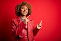 Young beautiful African American afro woman with curly hair wearing casual red jacket smiling and looking at the camera pointing Royalty Free Stock Photo