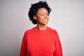 Young beautiful African American afro woman with curly hair wearing red casual sweater looking away to side with smile on face, Royalty Free Stock Photo