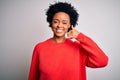 Young beautiful African American afro woman with curly hair wearing red casual sweater smiling doing phone gesture with hand and Royalty Free Stock Photo