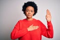 Young beautiful African American afro woman with curly hair wearing red casual sweater Swearing with hand on chest and open palm,