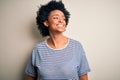 Young beautiful African American afro woman with curly hair wearing striped t-shirt looking away to side with smile on face, Royalty Free Stock Photo