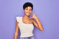 Young beautiful african american afro woman wearing casual t-shirt over purple background smiling doing phone gesture with hand Royalty Free Stock Photo