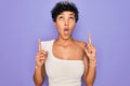 Young beautiful african american afro woman wearing tiara crown over purple background amazed and surprised looking up and Royalty Free Stock Photo