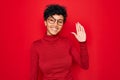 Young beautiful african american afro woman wearing turtleneck sweater and glasses Waiving saying hello happy and smiling,