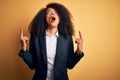 Young beautiful african american business woman with afro hair wearing elegant jacket amazed and surprised looking up and pointing Royalty Free Stock Photo