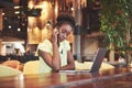 Young beautiful African-American business woman talking on the phone while working in a cafe Royalty Free Stock Photo