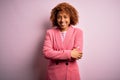 Young beautiful African American businesswoman with curly hair wearing elegant pink jacket happy face smiling with crossed arms Royalty Free Stock Photo