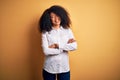 Young beautiful african american elegant woman with afro hair standing over yellow background happy face smiling with crossed arms Royalty Free Stock Photo