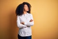 Young beautiful african american elegant woman with afro hair standing over yellow background looking to the side with arms Royalty Free Stock Photo