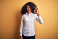 Young beautiful african american elegant woman with afro hair standing over yellow background smiling positive doing ok sign with Royalty Free Stock Photo