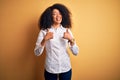 Young beautiful african american elegant woman with afro hair standing over yellow background success sign doing positive gesture Royalty Free Stock Photo