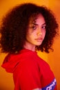 A young beautiful African-American girl in a red hoodie on a yellow isolated background in yellow lighting. small focus area