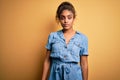 Young beautiful african american girl wearing denim dress standing over yellow background Relaxed with serious expression on face Royalty Free Stock Photo