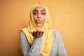 Young beautiful african american girl wearing muslim hijab over isolated yellow background looking at the camera blowing a kiss Royalty Free Stock Photo