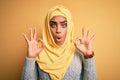 Young beautiful african american girl wearing muslim hijab over isolated yellow background looking surprised and shocked doing ok Royalty Free Stock Photo