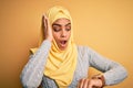 Young beautiful african american girl wearing muslim hijab over isolated yellow background Looking at the watch time worried,