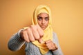 Young beautiful african american girl wearing muslim hijab over isolated yellow background Punching fist to fight, aggressive and