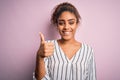 Young beautiful african american girl wearing striped t-shirt standing over pink background doing happy thumbs up gesture with Royalty Free Stock Photo