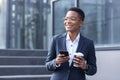 Young beautiful african american student with short hair, uses mobile phone happy and smiling walking in the city Royalty Free Stock Photo