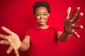 Young beautiful african american woman with afro hair over isolated red background looking at the camera smiling with open arms Royalty Free Stock Photo