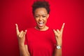 Young beautiful african american woman with afro hair over isolated red background shouting with crazy expression doing rock Royalty Free Stock Photo