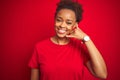 Young beautiful african american woman with afro hair over isolated red background smiling doing phone gesture with hand and Royalty Free Stock Photo