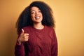 Young beautiful african american woman with afro hair standing over yellow isolated background doing happy thumbs up gesture with Royalty Free Stock Photo