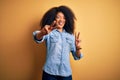 Young beautiful african american woman with afro hair standing over yellow isolated background smiling looking to the camera Royalty Free Stock Photo