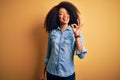 Young beautiful african american woman with afro hair standing over yellow isolated background smiling positive doing ok sign with Royalty Free Stock Photo