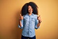 Young beautiful african american woman with afro hair standing over yellow isolated background success sign doing positive gesture Royalty Free Stock Photo