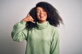 Young beautiful african american woman with afro hair wearing green winter sweater smiling doing phone gesture with hand and Royalty Free Stock Photo