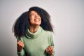 Young beautiful african american woman with afro hair wearing green winter sweater very happy and excited doing winner gesture