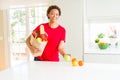 Young beautiful african american woman holding paper bag full of fresh healthy groceries leaving vegetables on the table Royalty Free Stock Photo