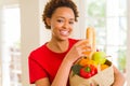 Young beautiful african american woman holding paper bag full of fresh healthy groceries and picking vegetables Royalty Free Stock Photo