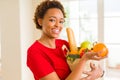 Young beautiful african american woman holding paper bag full of fresh healthy groceries and picking vegetables Royalty Free Stock Photo