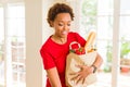 Young beautiful african american woman holding paper bag full of fresh healthy groceries and picking vegetables Royalty Free Stock Photo