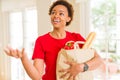 Young beautiful african american woman holding paper bag full of fresh healthy groceries and picking vegetables Royalty Free Stock Photo