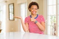 Young beautiful african american woman at home Showing palm hand and doing ok gesture with thumbs up, smiling happy and cheerful Royalty Free Stock Photo