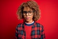 Young beautiful african american woman wearing casual shirt and glasses over red background with serious expression on face Royalty Free Stock Photo