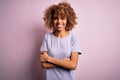 Young beautiful african american woman wearing casual t-shirt standing over pink background happy face smiling with crossed arms Royalty Free Stock Photo