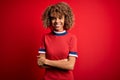 Young beautiful african american woman wearing casual t-shirt standing over red background happy face smiling with crossed arms Royalty Free Stock Photo