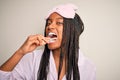 Young beautiful african american woman wearing pajama and sleep mask brushing her teeth using tooth brush and oral paste, cleaning Royalty Free Stock Photo