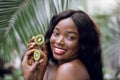 Young beautiful African woman with healthy glow perfect smooth skin, holds halfs of green kiwi fruit. Model with natural