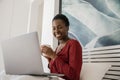 African woman sitting in bed holding coffee cup looking at laptop Royalty Free Stock Photo