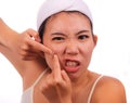 Young beautiful angry and upset Asian Korean woman with acne pooping head of pimple with her fingers on the mirror cleansing the Royalty Free Stock Photo